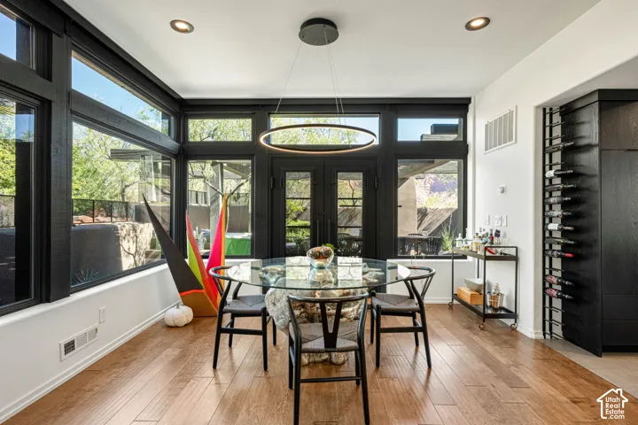 Floor-to-ceiling windows with black frames, integrated built-in wine storage, wood-finish flooring, recessed lighting, and a modern ring chandelier