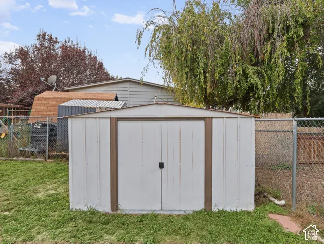 Metal storage shed with double doors, set within a fenced perimeter featuring mature trees
