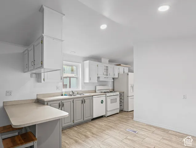 Kitchen featuring white upper cabinetry, grey lower cabinetry, integrated peninsula, neutral stone-finish countertops, and wood-finish flooring