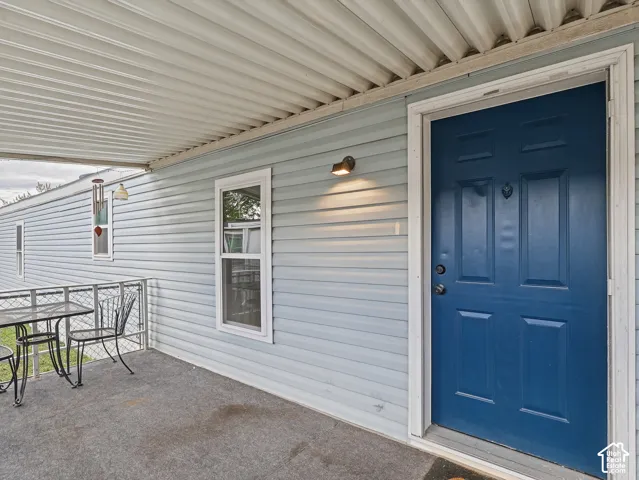 Covered exterior porch with light blue horizontal siding, solid blue entry door, and metal railing