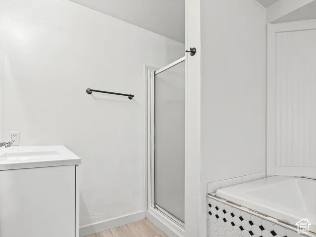 Bathroom featuring a white vanity with a neutral solid surface countertop, corner tub with a black and white geometric tile surround, glass-enclosed shower, and matte black hardware