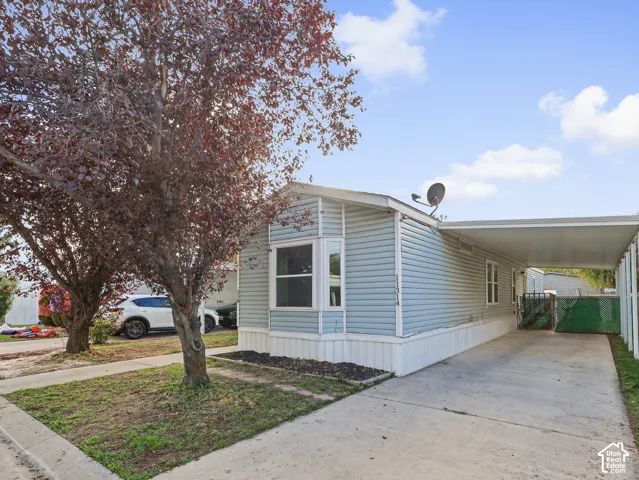 Light blue vinyl siding exterior featuring a bay window, attached carport, and mature landscaping
