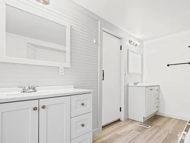 Dual white vanities featuring solid surface countertops, beadboard wall paneling, framed mirrors, and wood-finish flooring