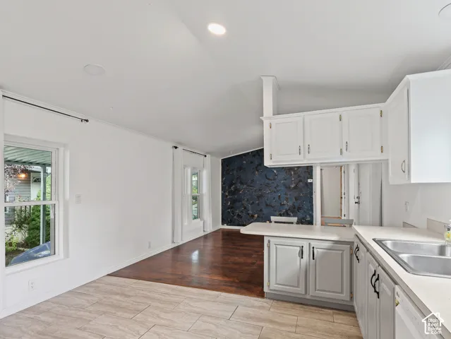 Open-concept interior featuring light-toned tile flooring, wood-finish flooring, white cabinetry with matte black hardware, dual-basin stainless steel sink, and a decorative dark accent wall
