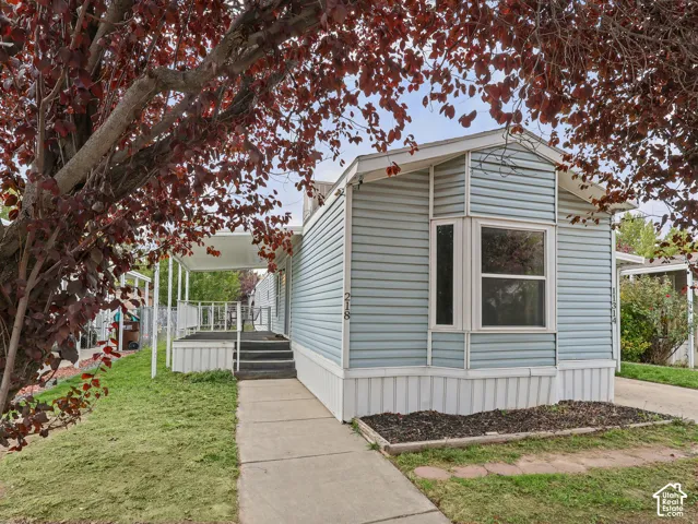 Exterior featuring horizontal light blue siding, a covered porch with metal railing, a concrete walkway, and a prominent bay window