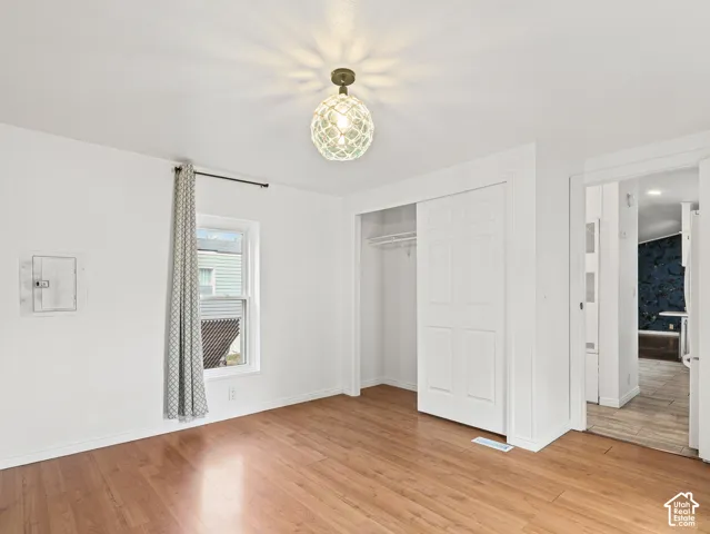 Room featuring wood-finish flooring, a spherical caged ceiling light fixture, a single-window pane with curtain rod, and a built-in closet with double-panel sliding doors