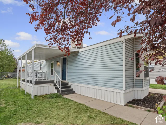 Exterior featuring light blue horizontal siding, a covered porch with metal railing, concrete walkway, and a bay window