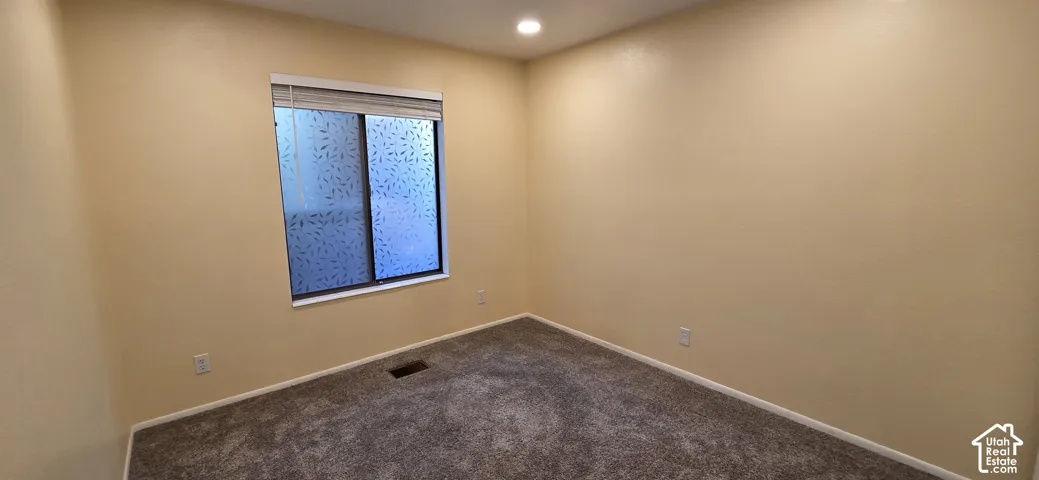 Neutral interior space featuring textured wall finishes, recessed ceiling lighting, wall-to-wall carpeting, and a sliding window with privacy-patterned glass