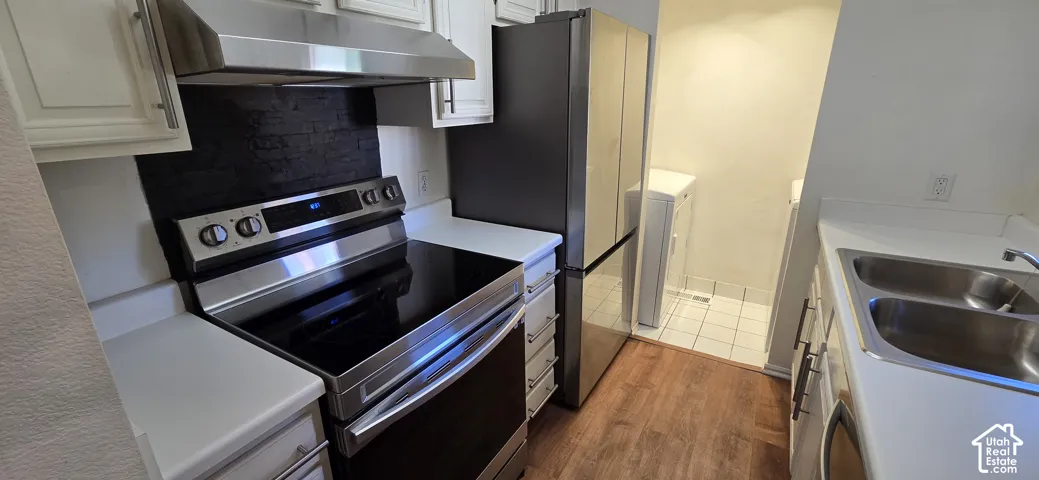 Kitchen featuring white cabinetry, solid-surface countertops, stainless steel appliances, a black tile backsplash, and wood-finish flooring