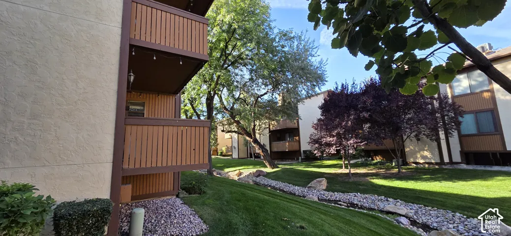 Exterior multi-level balconies with vertical wood-finish siding, set against mature trees, landscaped lawns, and stone-lined drainage features