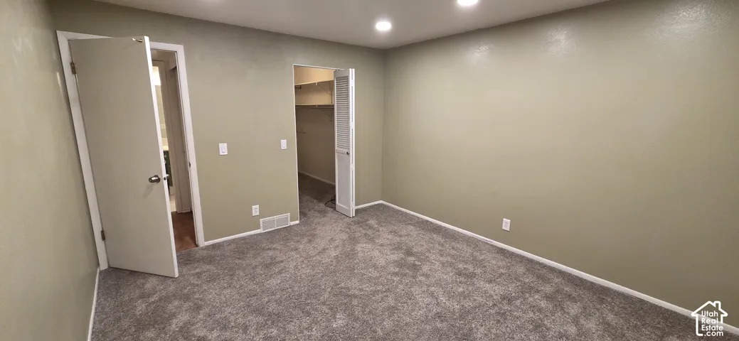 Neutral-toned interior space featuring wall-to-wall carpeting, recessed ceiling lighting, and two interior doorways, one with louvered double doors providing access to a storage area
