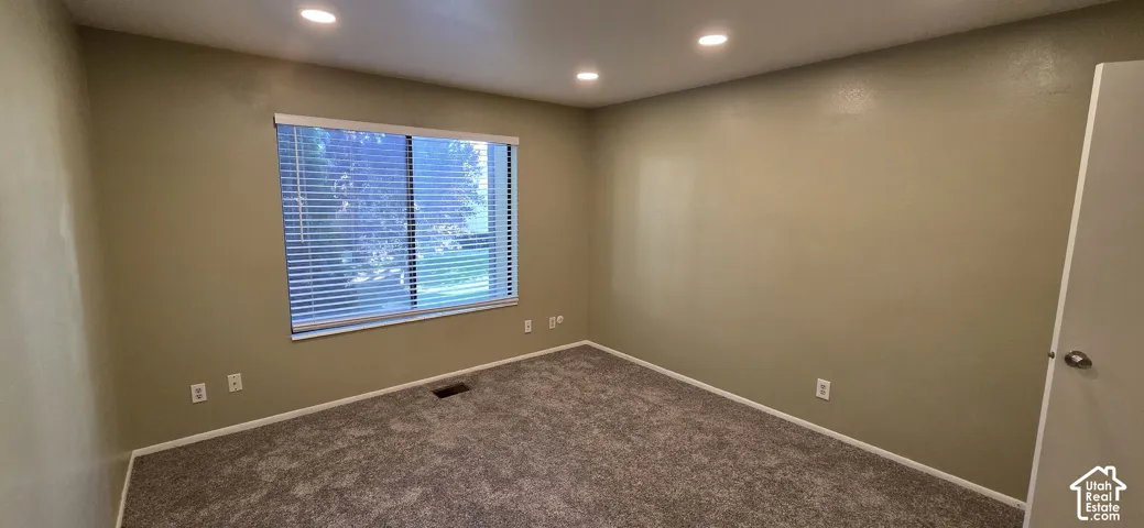 Neutral-toned interior room featuring wall-to-wall carpeting, recessed ceiling lighting, and a window with horizontal blinds
