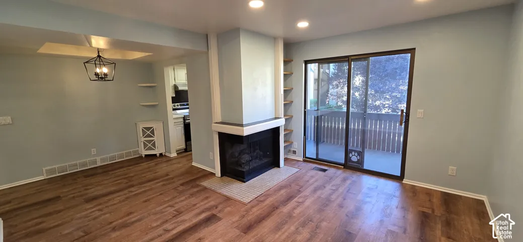 Wood-finish flooring, corner fireplace with a stone hearth, recessed ceiling lighting, built-in shelving, and sliding glass doors