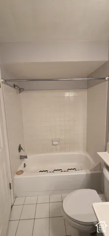 Bathtub and shower combination featuring a white tile surround, integrated soap dish, and metal shower hardware, finished with white floor tiling