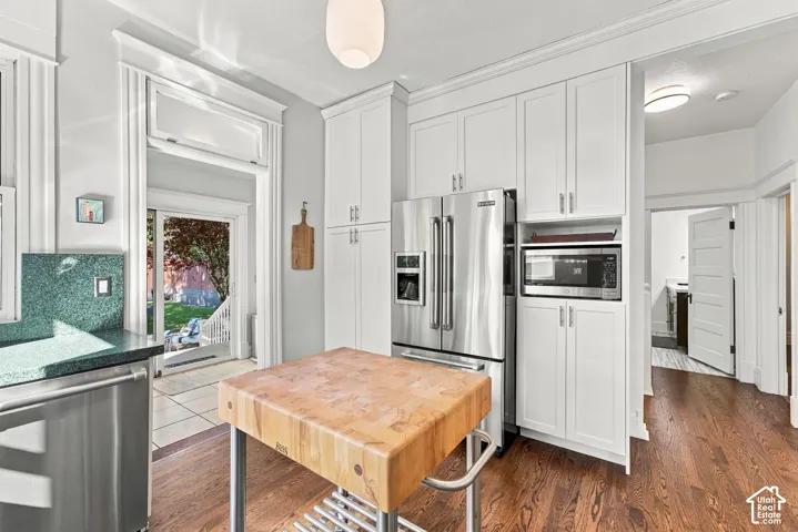 Kitchen featuring full-height white shaker cabinetry, stainless steel appliances, wood-finish flooring, and crown molding
