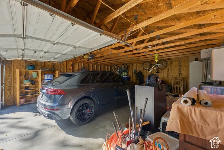 Multi-car garage featuring concrete flooring, exposed wooden truss ceiling, and an overhead automatic door