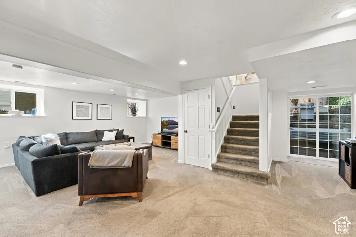 Neutral-toned interior space featuring recessed lighting, carpeted flooring, sliding glass doors with grid detailing, and a carpeted staircase with a white handrail