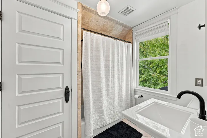 Bathroom featuring a pedestal sink with matte black faucet, stone tile shower surround, and a multi-panel interior door with oil-rubbed bronze hardware