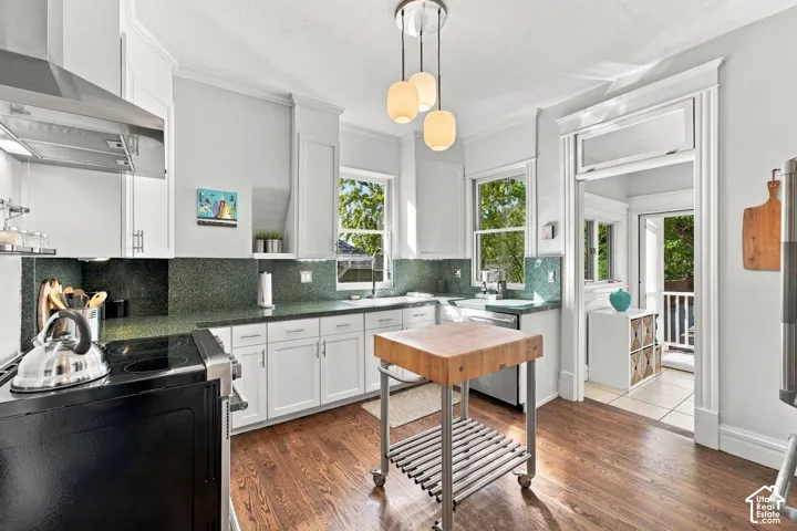 Kitchen featuring white shaker-style cabinetry, green stone-finish countertops, wood-finish flooring, a stainless steel range hood, and a trio of pendant lights