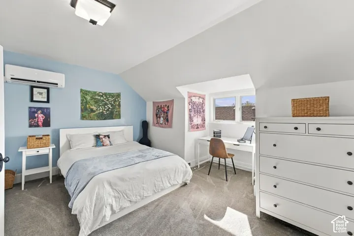Vaulted ceilings, wall-mounted ductless climate control unit, carpeted flooring, and a multi-pane window