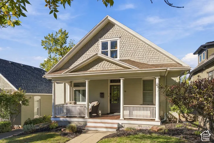 Exterior featuring a covered front porch with white columns and railings, gable roofline, light-colored brick siding, and shingle-style gable detailing