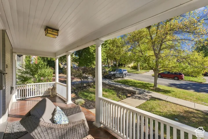 Covered front porch featuring wood-finish flooring, white spindle railings, classic support columns, and an inset ceiling fixture