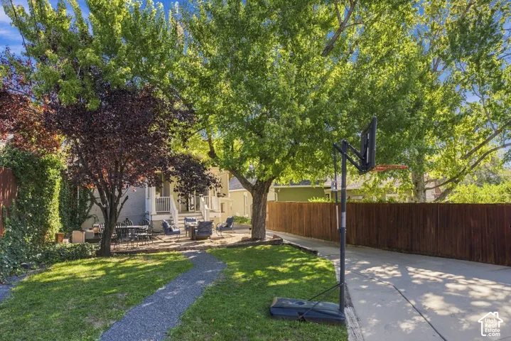 Backyard space featuring a stone patio, mature trees, gravel pathway, and perimeter wood fencing