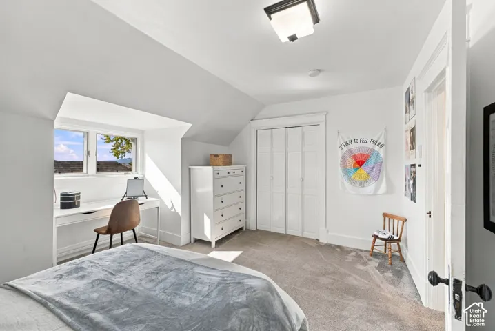Bedroom featuring vaulted ceilings, a window-inset alcove, carpeted flooring, and a closet with bifold doors