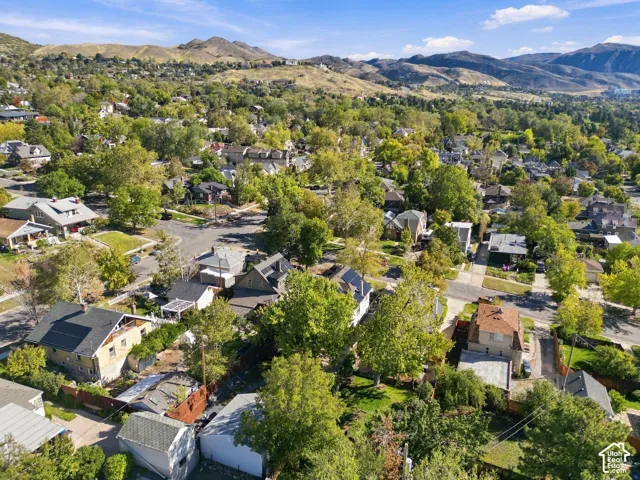 Aerial perspective of a neighborhood featuring mature deciduous trees, grid-patterned streets, and a prominent mountain range backdrop