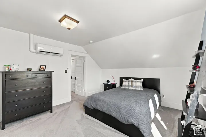 Room featuring sloped ceilings, wall-mounted climate control unit, five-panel interior door, and neutral carpeting