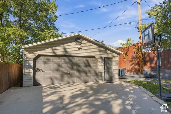 Detached garage featuring light-toned horizontal siding, a panelled overhead door, a dedicated pedestrian side entry, and concrete driveway apron