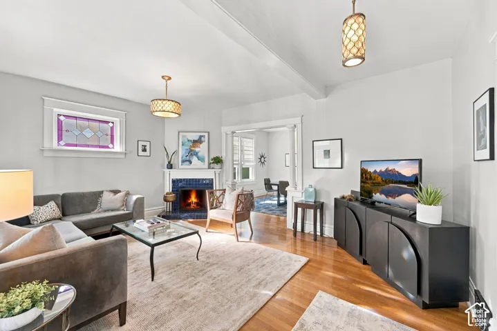 Living area featuring wood-finish flooring, a corner fireplace with decorative tile surround, crown molding, stained glass accent window, and two drum-style pendant light fixtures