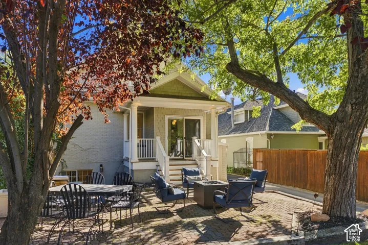 Rear exterior featuring a covered porch with white railing, brick paver patio, and mature tree canopy