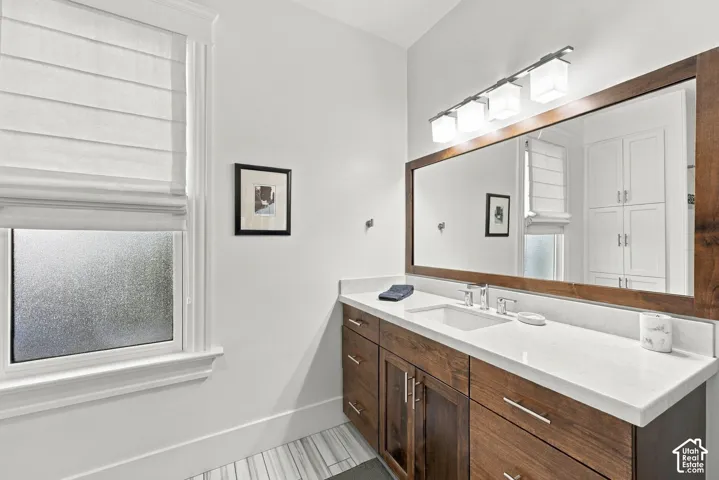 Bathroom vanity featuring a stained-wood cabinet, stone-finish countertop with an integrated rectangular sink, large-format mirror with a wood frame, and a four-light fixture