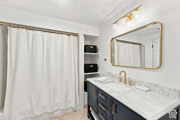 Navy blue vanity cabinet with stone-finish countertop, undermount sink, brass-tone hardware, arched-corner vanity mirror, and three-bulb vanity light fixture