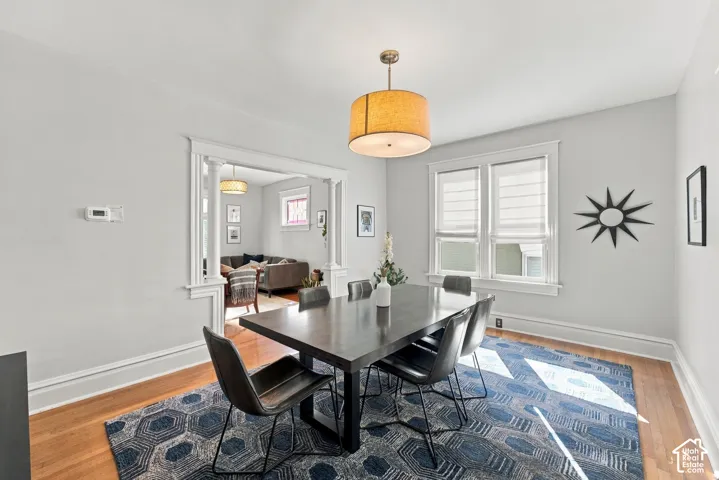 Formal dining area featuring wood-finish flooring, architectural cased opening with decorative columns, large drum-style pendant light fixture, and double-hung windows with white casing
