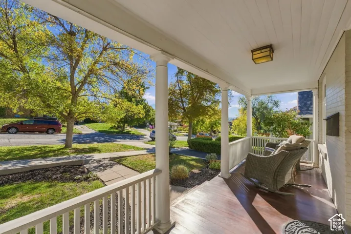 Covered front porch featuring wood-finish flooring, white railing, structural columns, and a flush-mount light fixture