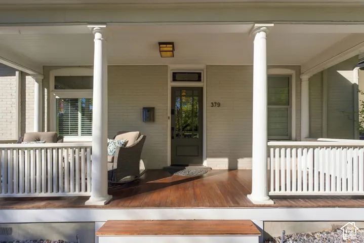 Covered front porch featuring wood-finish flooring, classical columns, a white balustrade, and a glass-paneled entry door with transom window