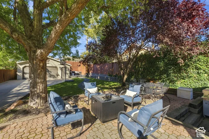 Private backyard featuring a paved stone patio, mature trees, lawn, detached two-car garage, and solid perimeter fencing