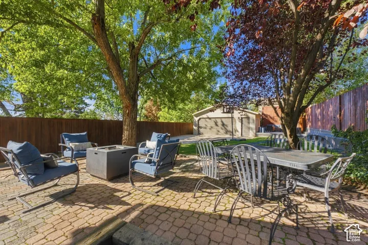 Backyard featuring a paved brick patio, mature trees, wood privacy fencing, and a detached two-car garage
