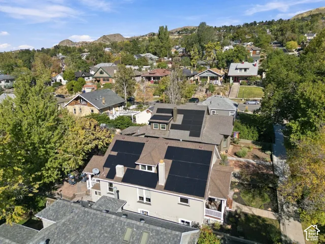 Aerial perspective of a multi-story residence featuring comprehensive roof-mounted solar panels, multiple brick chimneys, a shingle roof, and exterior masonry accents