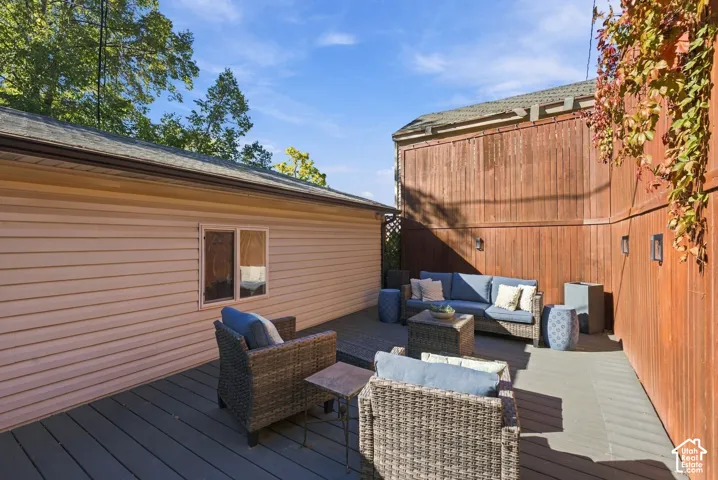 Outdoor deck featuring composite decking, vertical wood-plank fencing, wall-mounted exterior lighting, and a single-story structure with horizontal siding