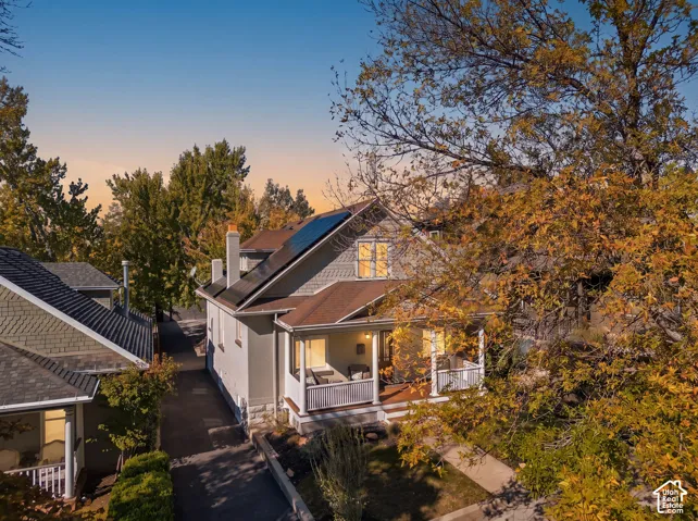 Exterior featuring a covered front porch with a railing, shingle siding, a pitched roofline, stone foundation detailing, and installed solar panels