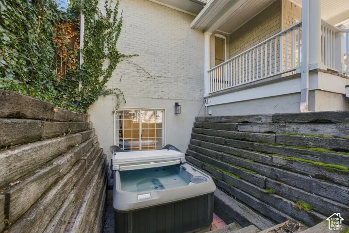 Exterior space featuring tiered timber retaining walls, an integrated hot tub, a recessed window, and an elevated porch with white railing