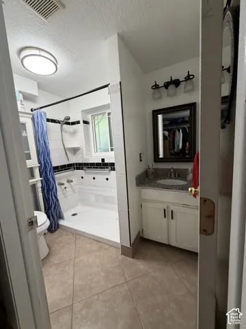 Bathroom featuring a tiled shower enclosure with black accent detailing, a vanity with a stone-surface countertop, an undermount sink, and three-light wall-mounted fixture