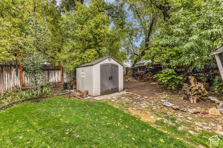 Backyard featuring a synthetic storage structure, stone-paver hardscaping, mature trees, and wooden perimeter fencing