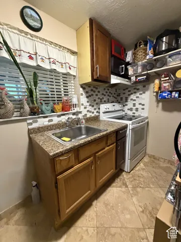 Kitchen area featuring medium-tone wood cabinetry, laminate countertops, a geometric mosaic tile backsplash, a stainless steel sink with a high-arch faucet, and tile flooring