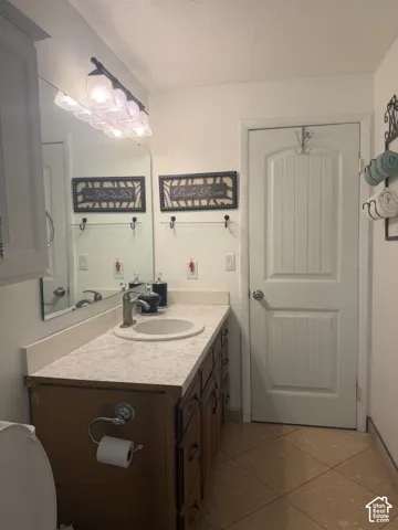 Vanity featuring a light-toned countertop with an integrated basin, wood-finish cabinetry, a large wall-mounted mirror, a four-light fixture, and ceramic tile flooring