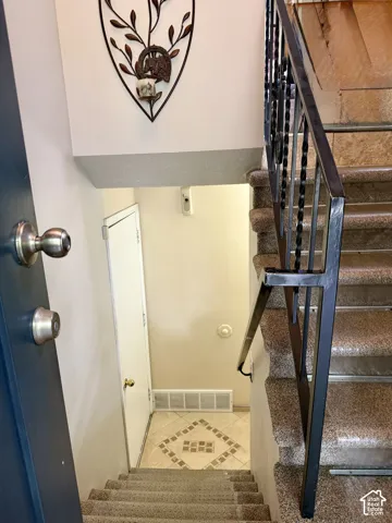 Staircase featuring textured stone-finish steps and a black metal railing with ornate balusters, landing on a tile floor with geometric inset detailing