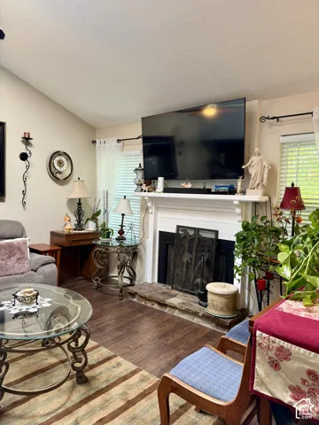 Living area featuring wood-finish flooring, vaulted ceilings, and a fireplace with a white mantel and stone hearth